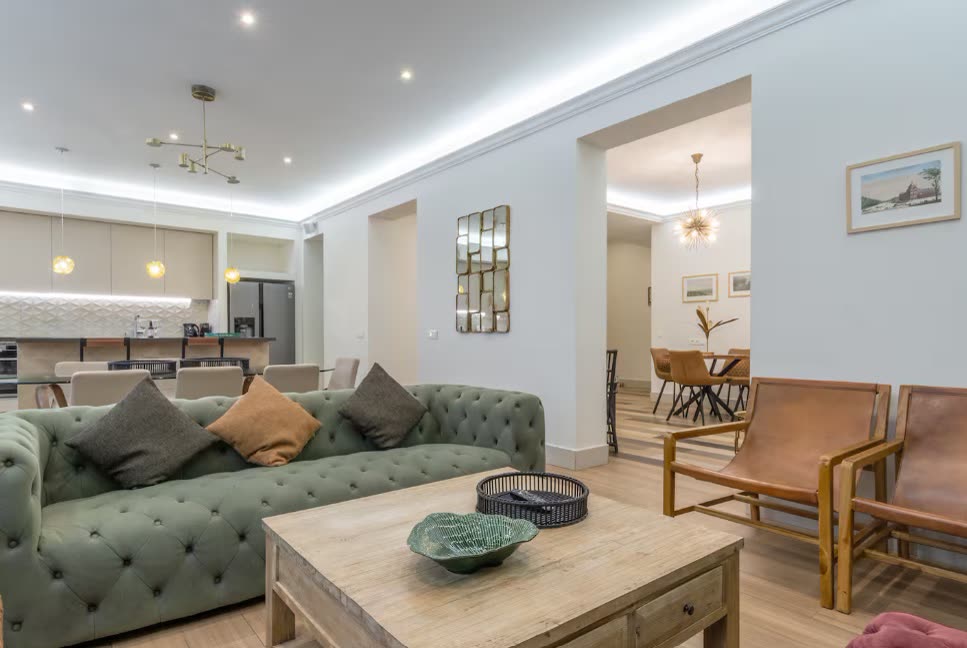 Open-plan living room with a green tufted sofa, leather armchairs and a wooden coffee table