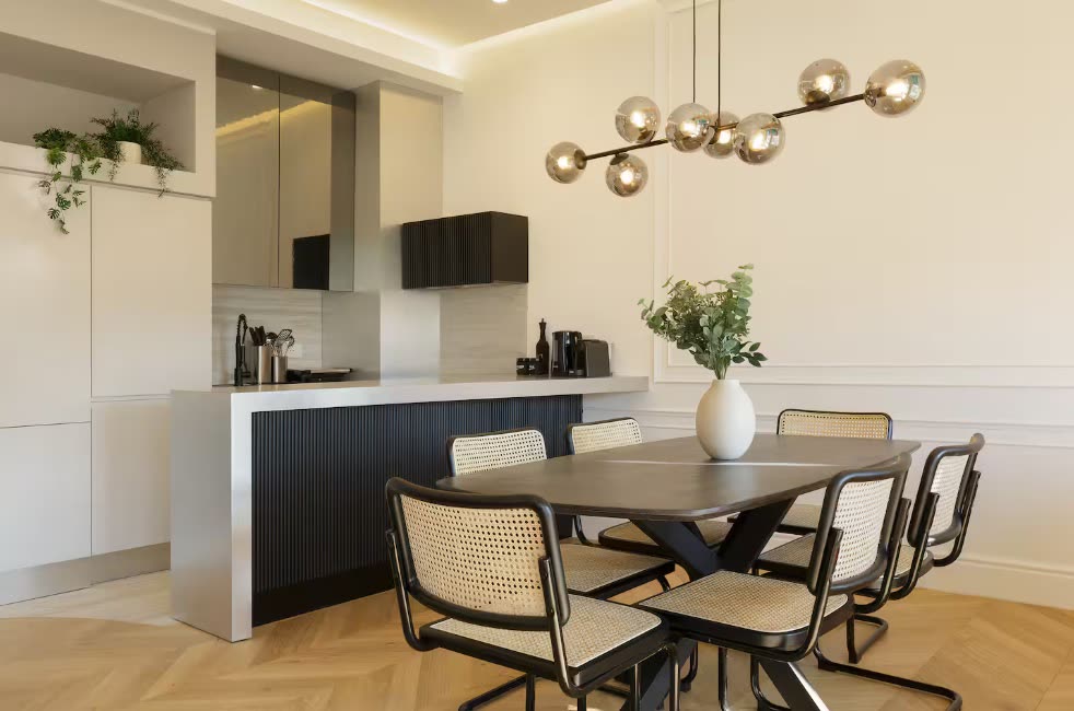 Modern kitchen and dining area with rattan chairs, a dark oval table and a globe pendant light